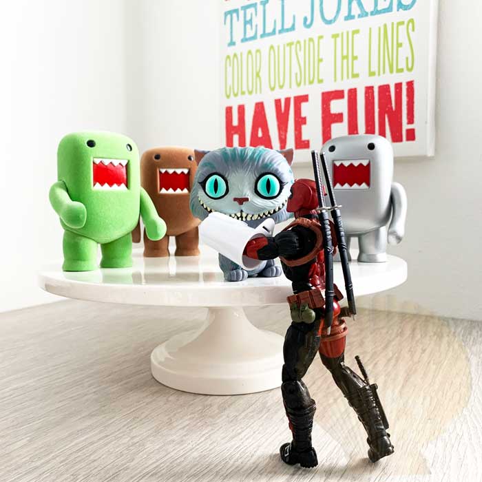 Deadpool uses a pet finger toothbrush to brush Funko Pop Cheshire Cat's teeth while other Domo figures wait their turn.